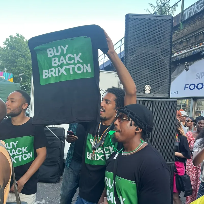 A supporter lifting a Buy Back Brixton placard beside the sound system.
